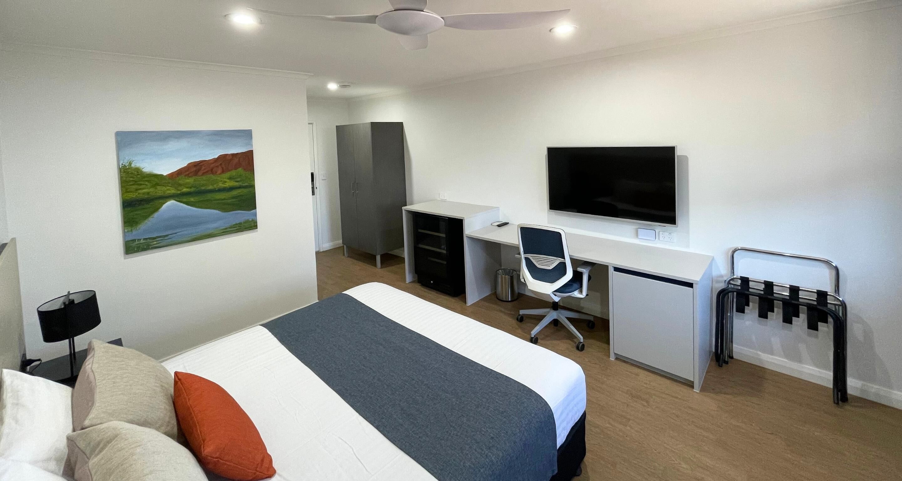 A hotel room with a bed, desk, chair, TV, and a painting on the wall.