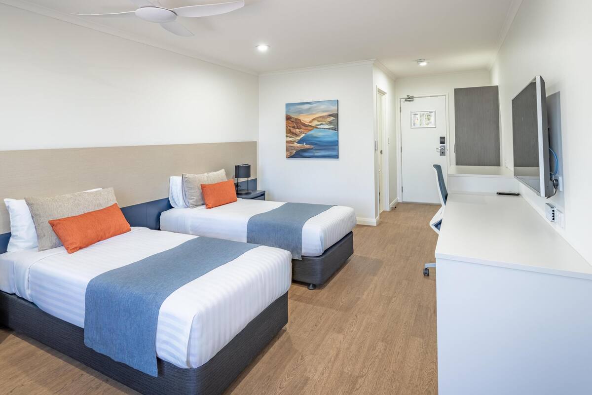 Ett hotellrum med två sängar, ett skrivbord, en tv och en tavla på väggen.