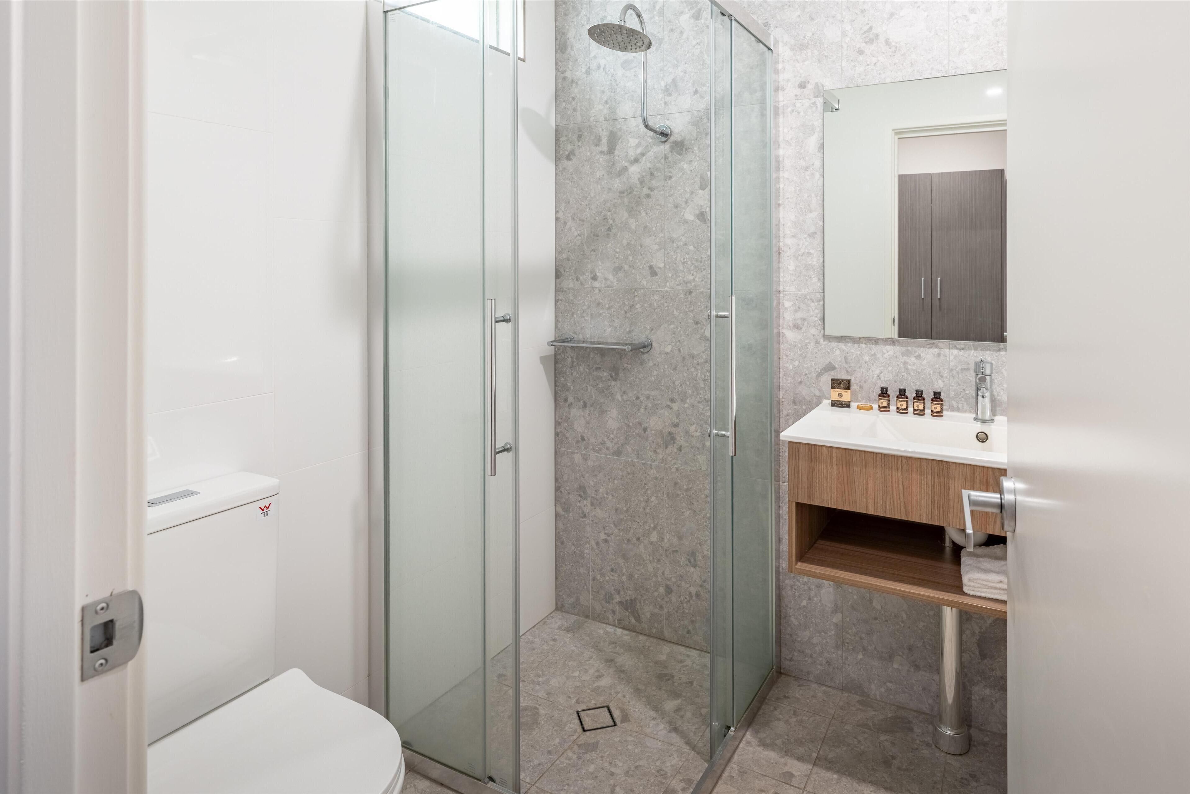 Un baño moderno con ducha de vidrio, inodoro y tocador con espejo.