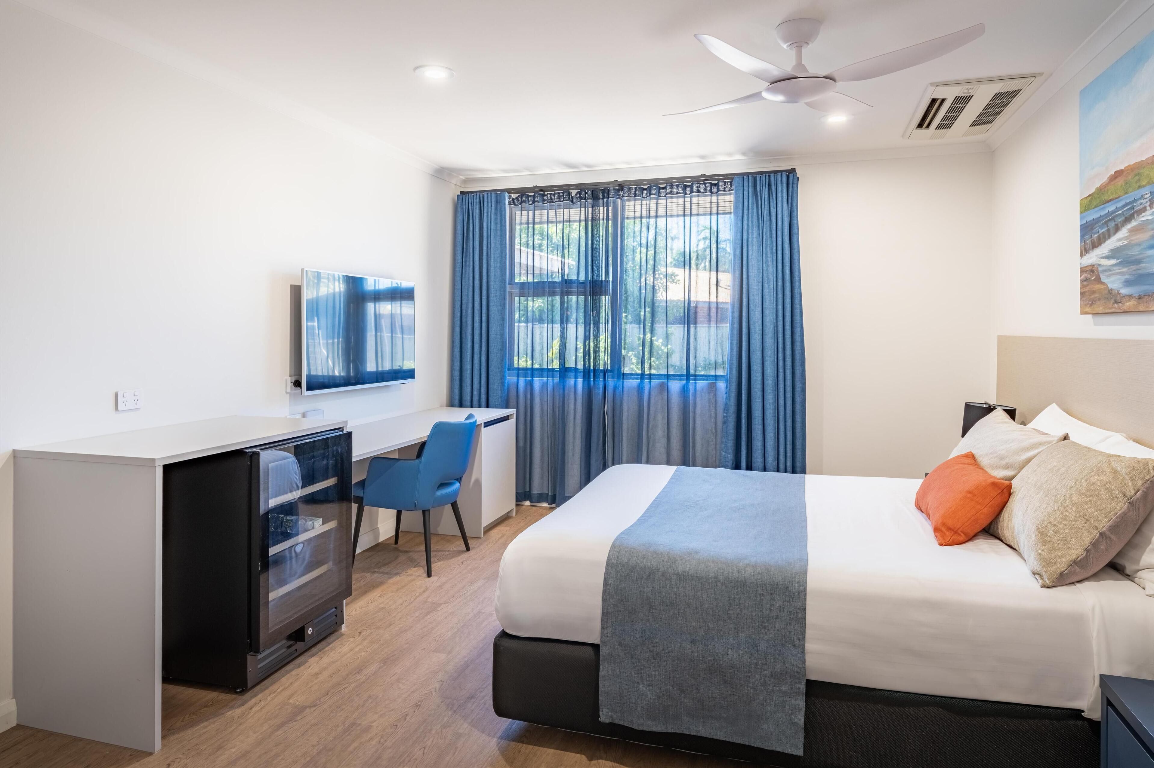 Una habitación de hotel con cama, escritorio, silla y televisor.