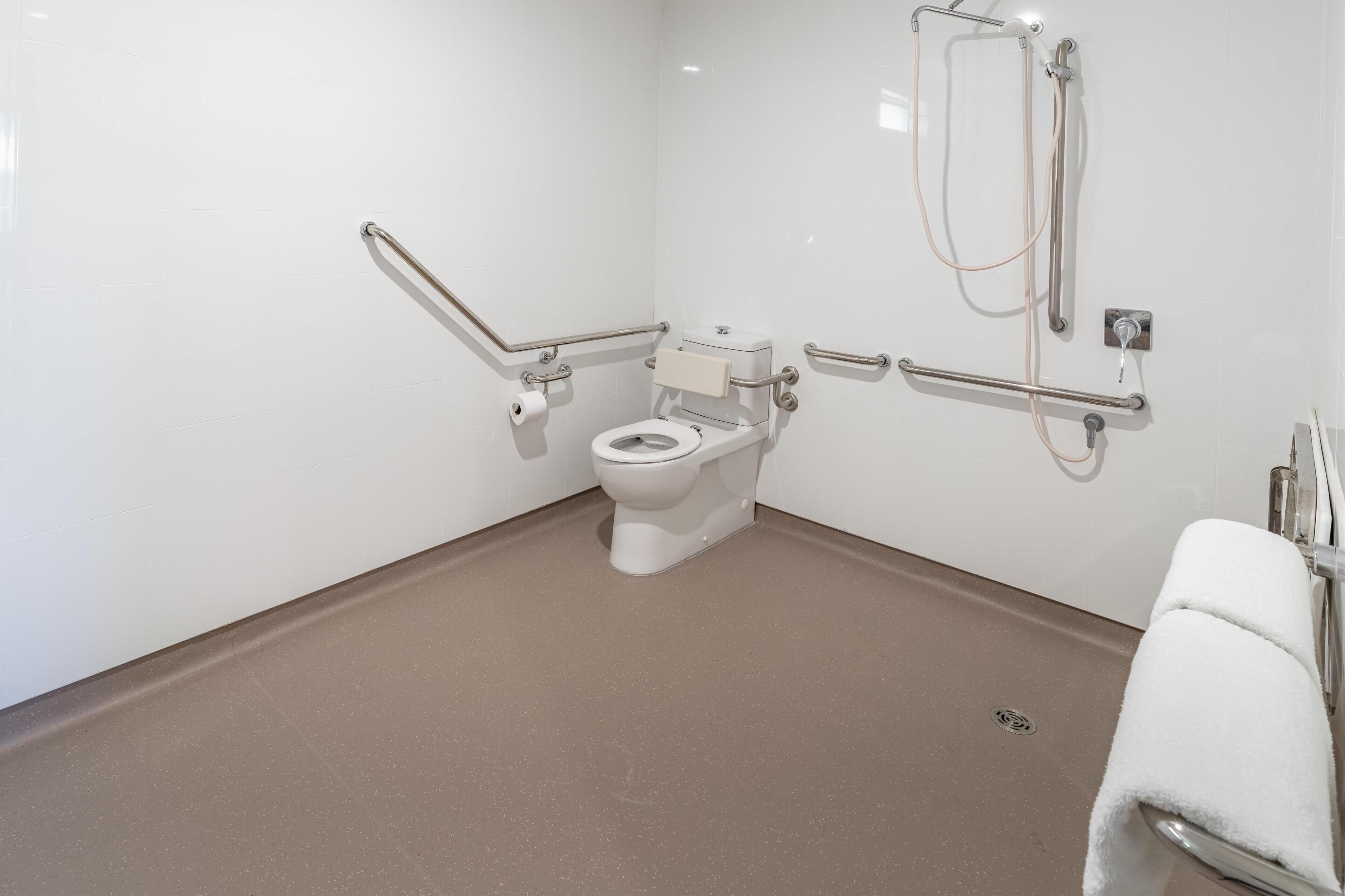 A wheelchair-accessible bathroom with a toilet, grab bars, and a shower.