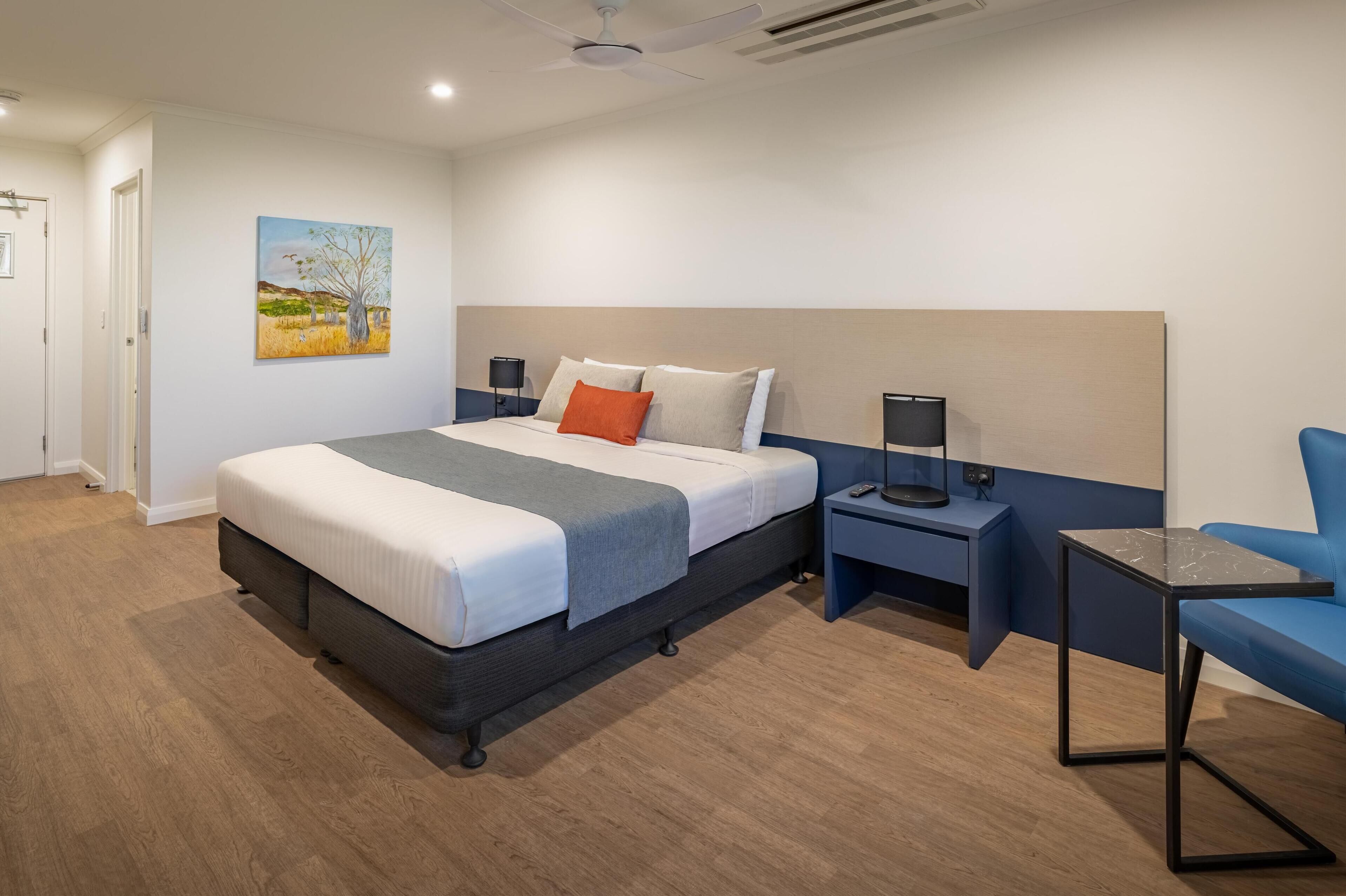 Una habitación de hotel moderna con una cama grande, un escritorio, una silla y un cuadro en la pared.
