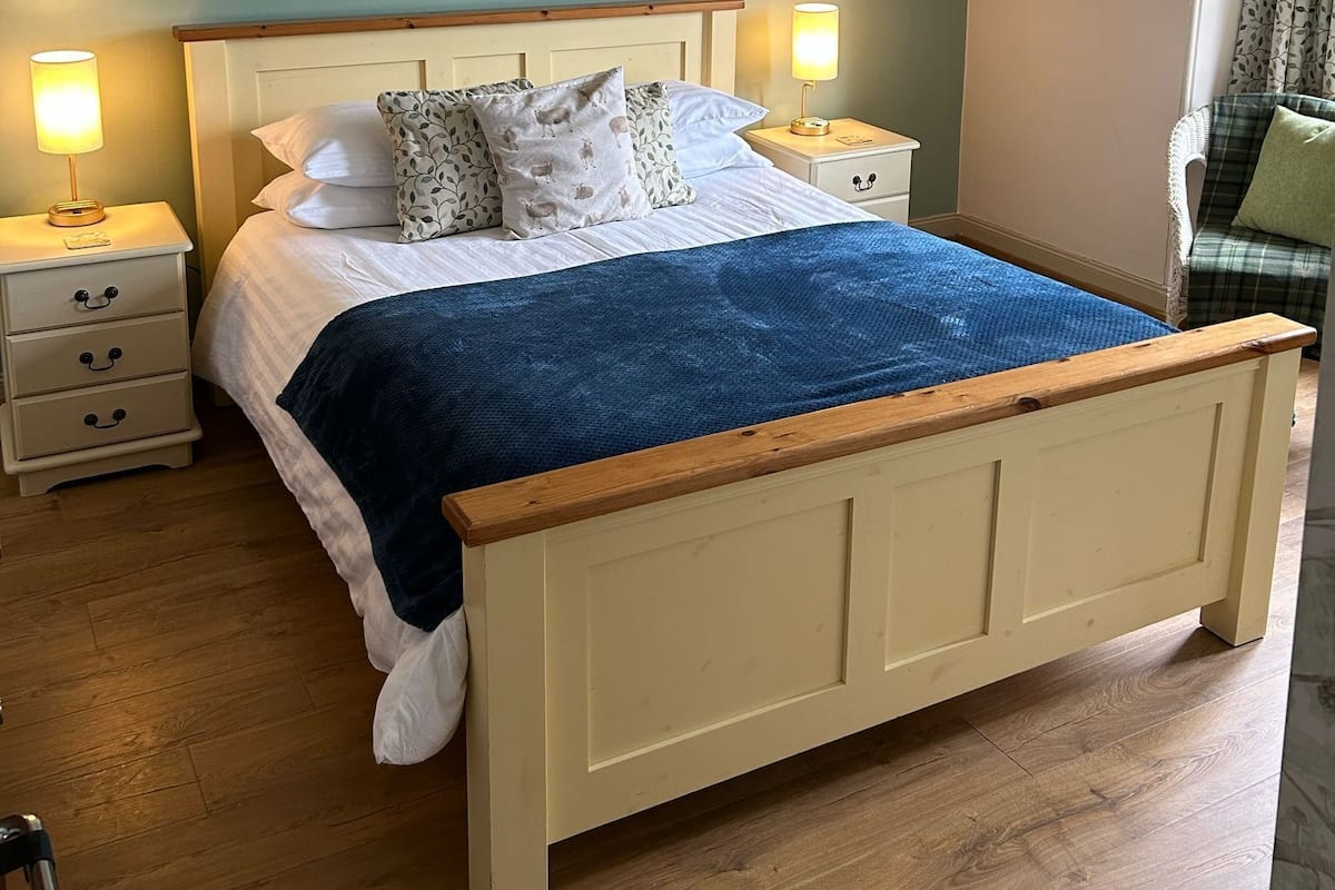 Une chambre à coucher avec un lit en bois, deux tables de chevet avec des lampes, une couverture bleue et deux œuvres d’art accrochées au mur.
