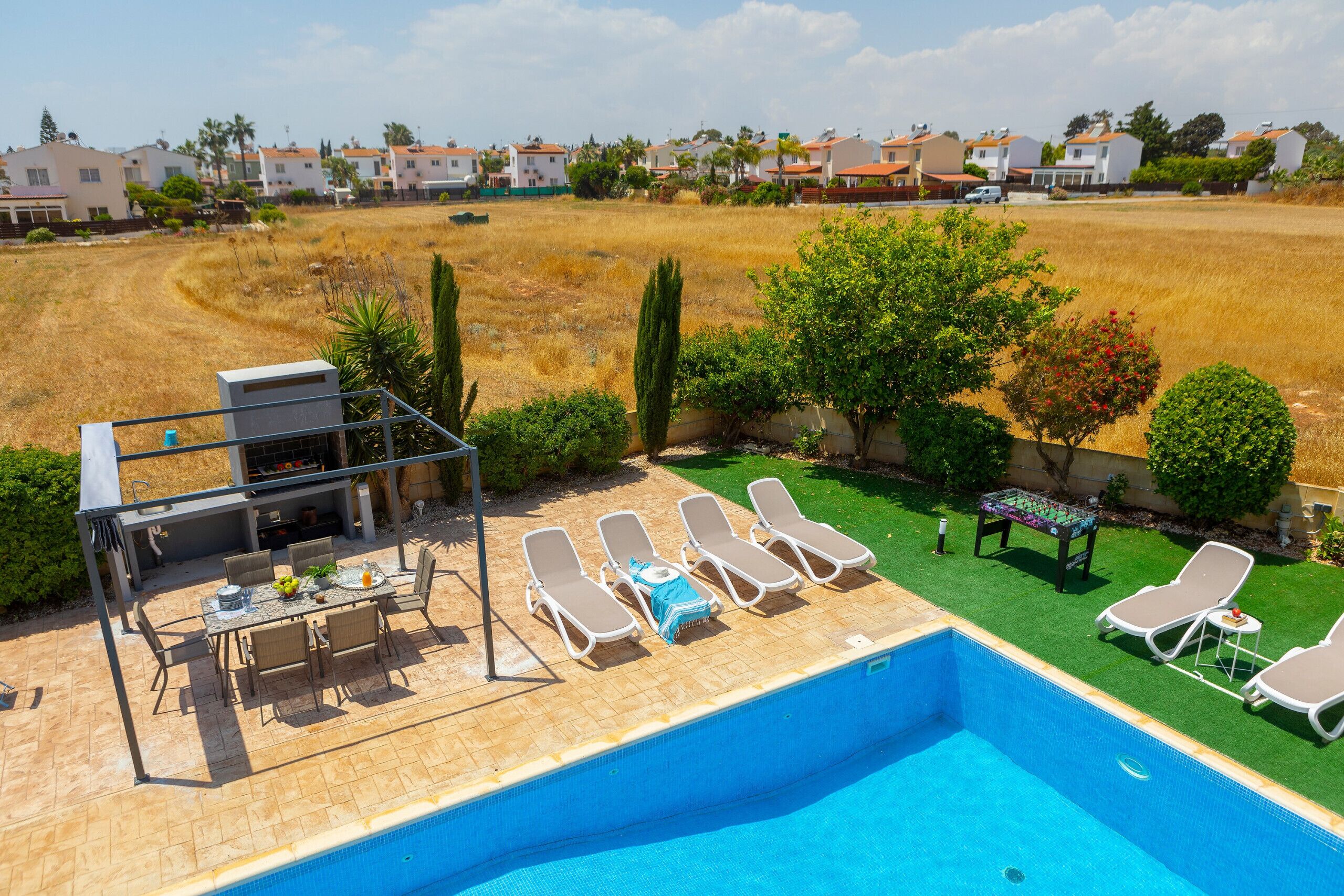 Quintal com piscina, espreguiçadeiras, área de churrasco e vista para uma área residencial.