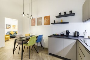 Eine moderne Küche mit Essbereich, mit einem Tisch, Stühlen, einer Kaffeemaschine und einem Wasserkocher auf der Arbeitsfläche.