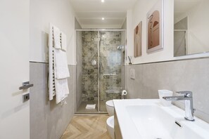 Ein modernes Badezimmer mit einer in Glas abgeschlossenen Dusche, einem weißen Waschbecken und einem großen Spiegel.