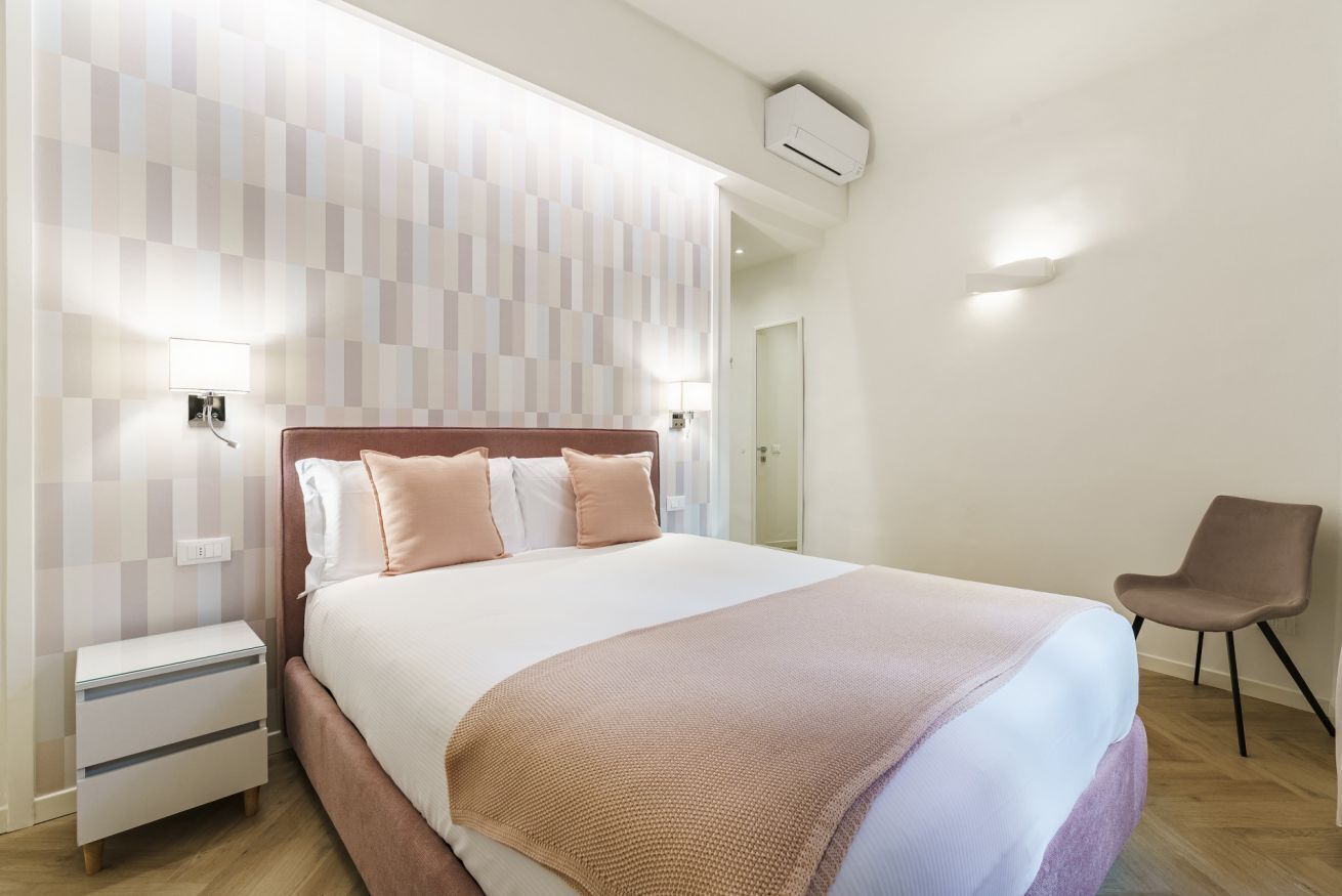 Une chambre d’hôtel moderne avec un grand lit, une table de chevet, une chaise et un climatiseur fixé au mur.