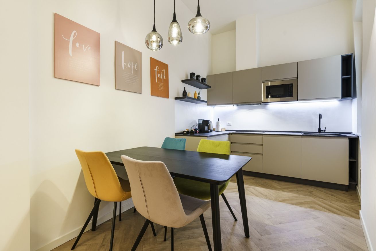 A modern kitchen with a dining area, featuring a wooden table, chairs, and pendant lights.