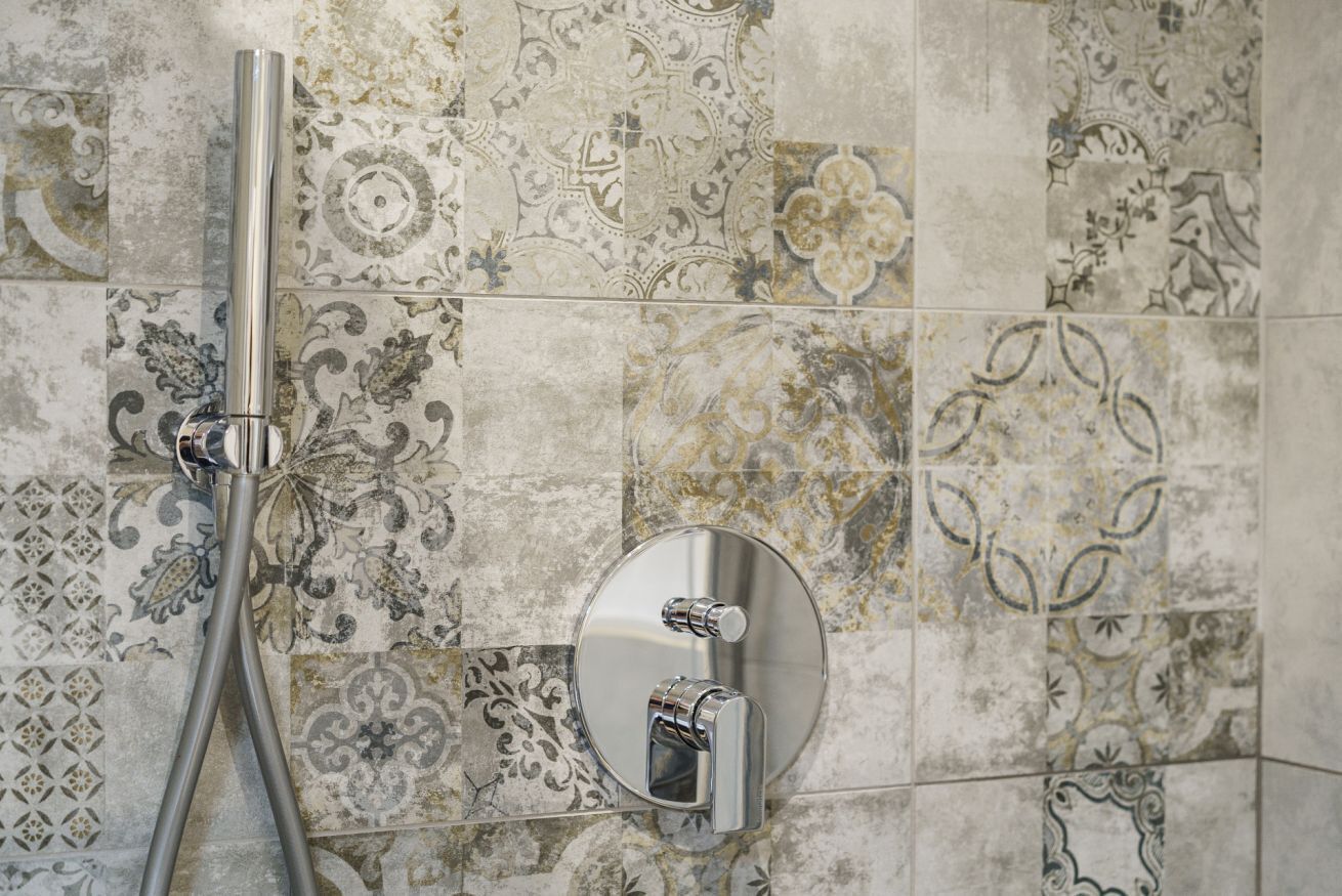 A shower with a chrome faucet and wall-mounted controls, set against a patterned tile backsplash.