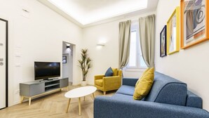 A modern living room with a sofa, a TV, a small table, and a potted plant. - Designer Apartment in Oltrarno (Firenze)