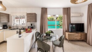 Cozinha moderna com ilha central, área de refeições e televisão sobreposta a um armário de madeira.