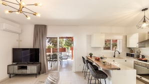 Una cocina moderna con televisor, taburetes de bar y un comedor con mesa y sillas.