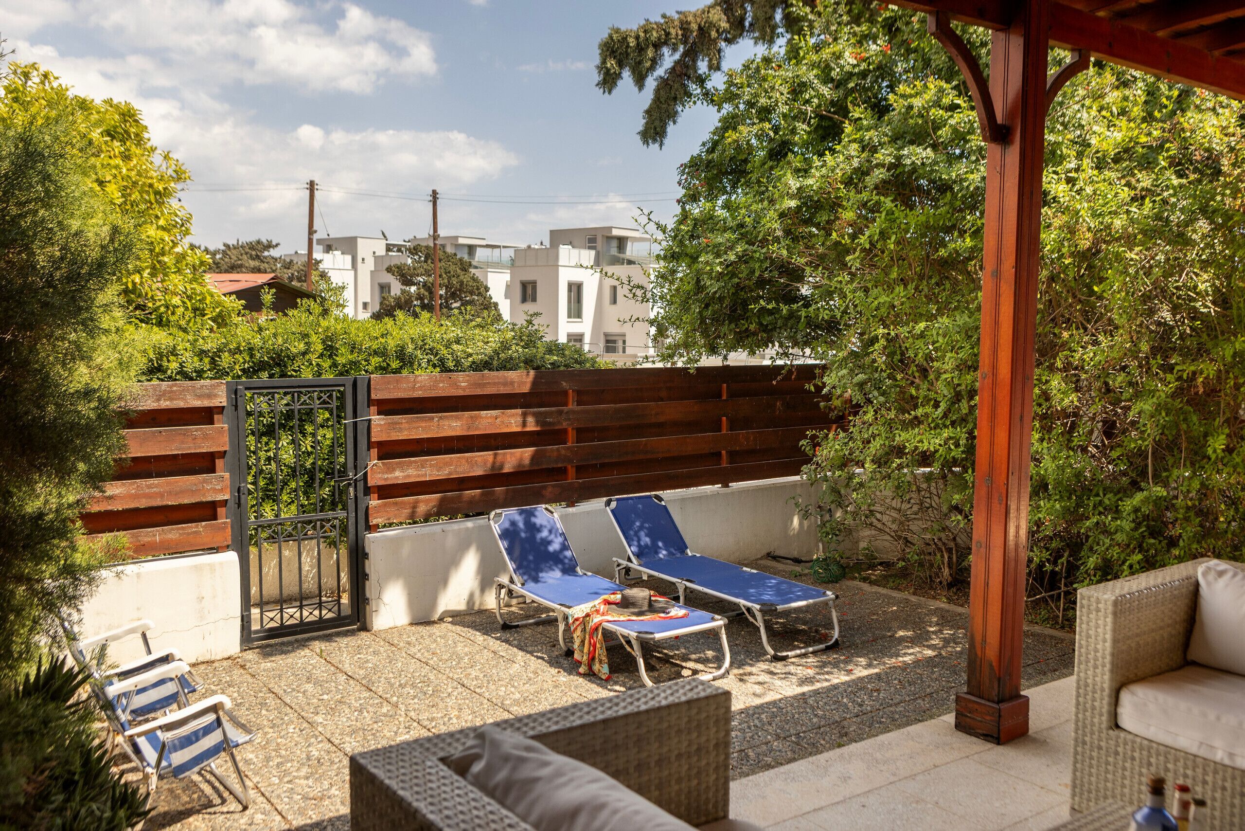 Een terras met twee lounge fauteuils, een rieten bank en een houten pergola.