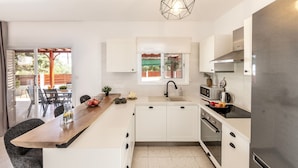Una cocina moderna con armarios blancos, encimera de madera, refrigerador de acero inoxidable y ventana con vista a un patio.