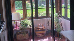 A room with a sliding glass door leading to a garden. There is a lamp, a basket, and a table with plants. - Charming F2 on the ground floor of a large house near Giverny (Lommoye)