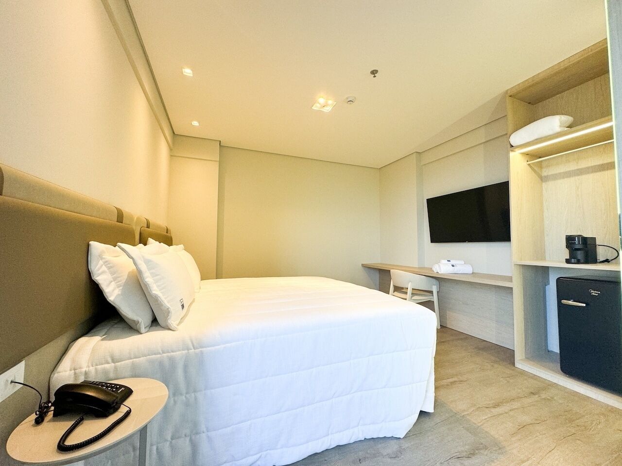 A hotel room with a bed, bedside table, TV, and a mini-fridge.