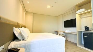 A hotel room with a bed, bedside table, TV, and a mini-fridge.
