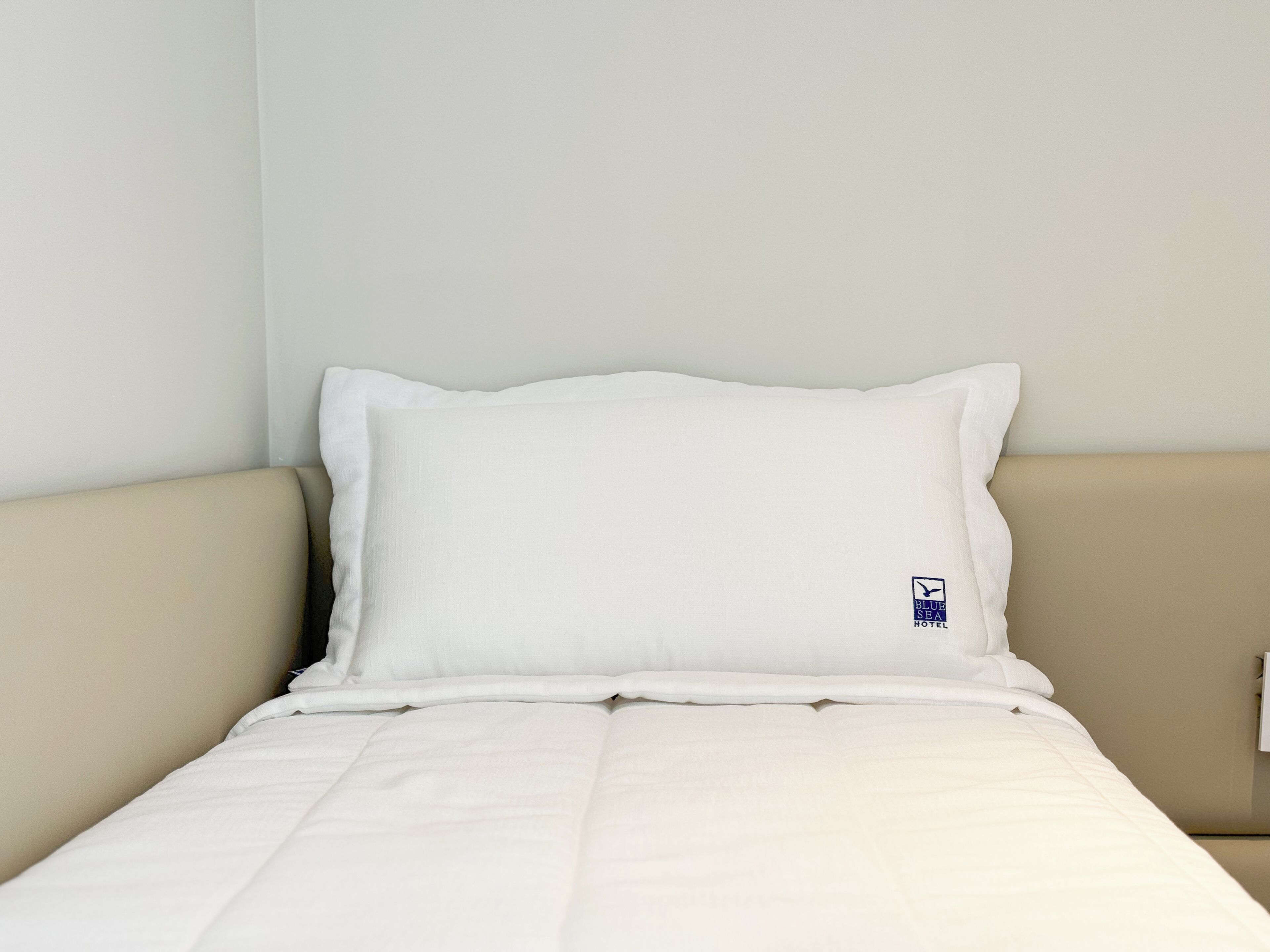 A neatly made bed with a white pillow and a small logo on the pillow.