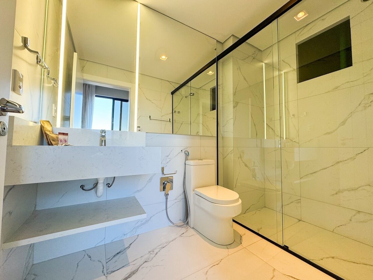 A modern bathroom with a glass shower enclosure, a white toilet, and a marble-tiled floor.