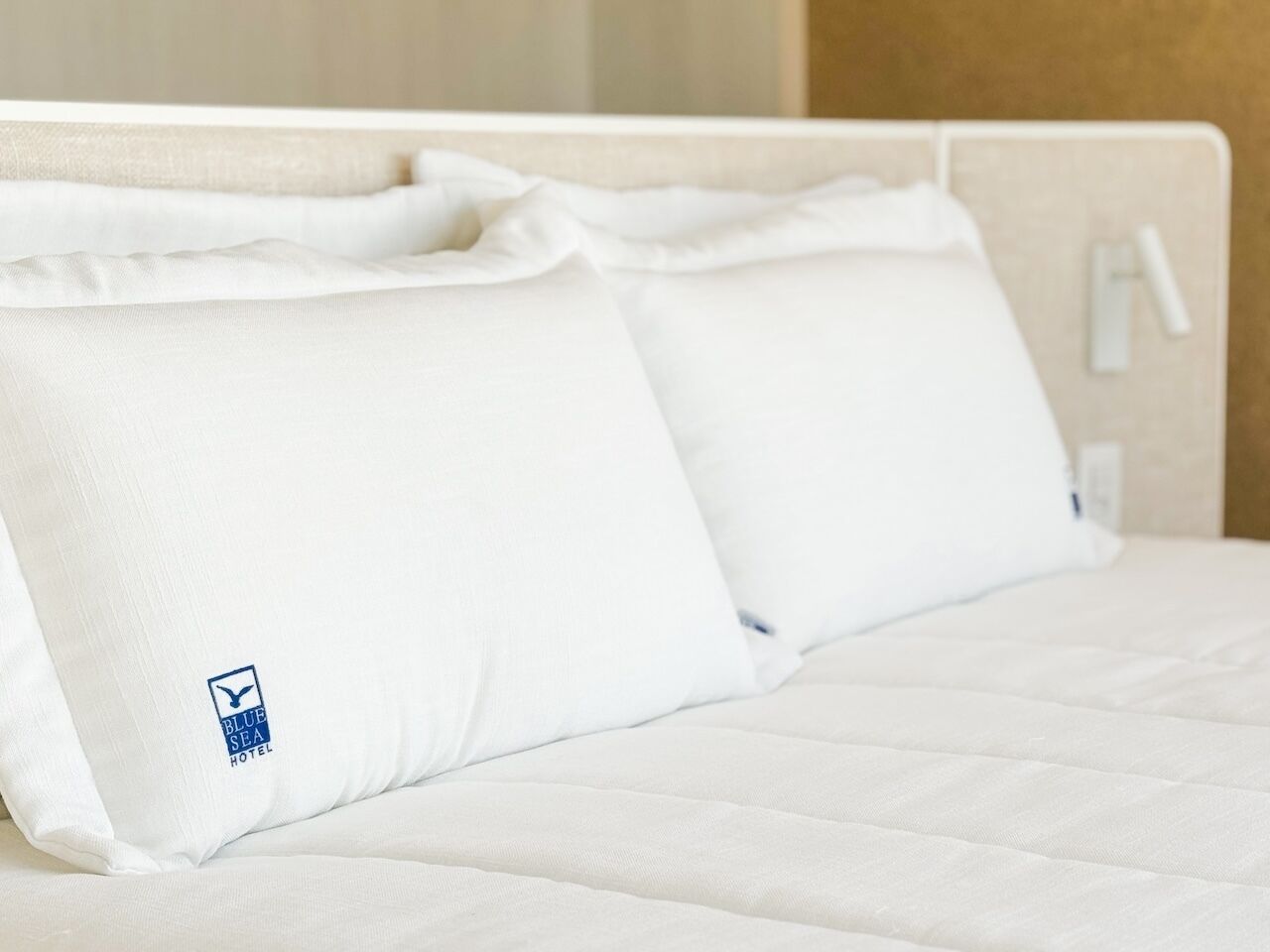 Una cama con ropa de cama y almohadas blancas, cabecera blanca y un pequeño logotipo en la almohada.