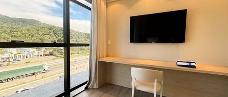 Habitación de hotel con un ventanal grande que ofrece vistas a una carretera y vegetación.
