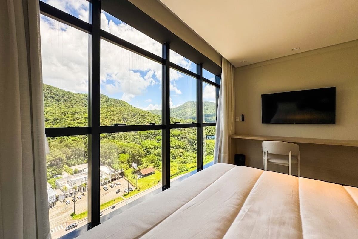 Habitación de hotel con un ventanal grande que ofrece vistas a un paisaje verde y un pueblo en la falda.