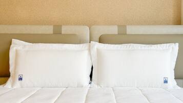 Una cama bien hecha con sábanas y almohadas blancas, un cabecero color beige y una pared texturizada en tono beige.