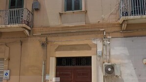 Un immeuble avec une porte à deux battants de couleur marron, un petit balcon doté de rampes en métal et un appareil de climatisation fixé au mur.