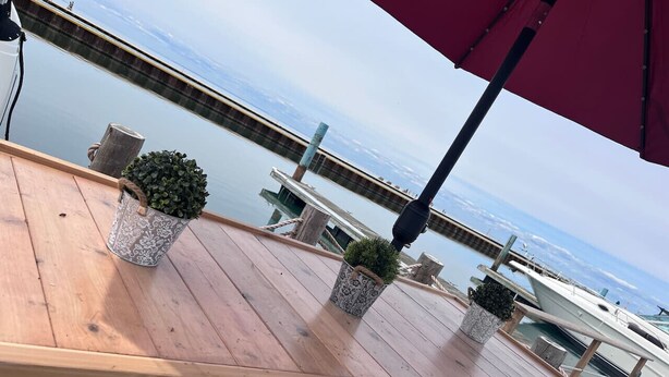 A wooden deck with potted plants and a red umbrella, overlooking a marina with boats. - Bob's Yer Uncle in Port Dalhousie (St. Catharines)