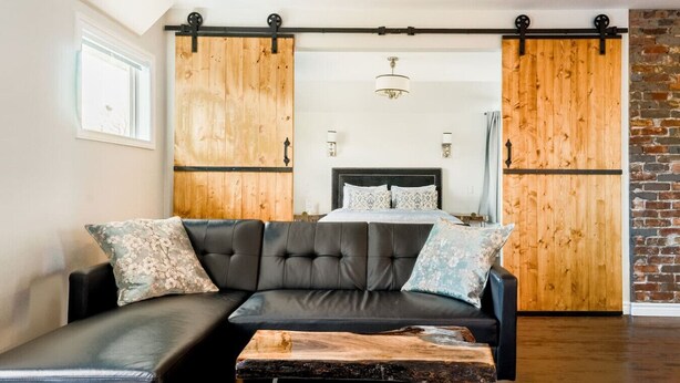 A modern living room with a sectional sofa, a wooden coffee table, and a bed with a headboard. - Stylishly Remodeled Queen Victoria Loft (Niagara Falls)