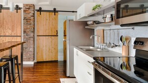 A modern kitchen with a wooden accent wall, a black countertop, and stainless steel appliances. - Stylishly Remodeled Queen Victoria Loft (Niagara Falls)