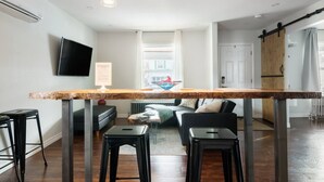 Un espace de vie moderne comprenant un comptoir de cuisine, des tabourets de bar, un téléviseur à écran plat et une porte coulissante de style rustique.