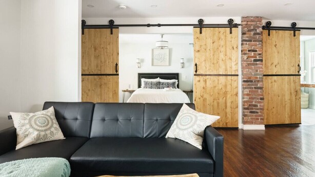 Un salon moderne avec un canapé en cuir noir, des portes coulissantes en bois et un mur d’accent en briques.
