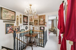 A hallway with a staircase, a chandelier, and various framed artworks on the walls.