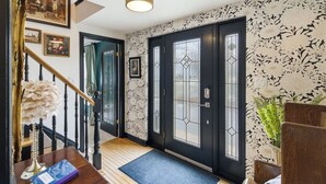Ein Flur mit einer Treppe, einer schwarzen Tür mit Glasfeldern und einer Wand mit floralen Mustern.