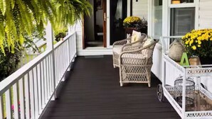 Eine überdachte Veranda mit Korbmöbeln, einem Blumentopf und einem kleinen Tisch mit Blumen.