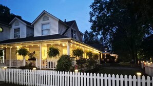 A two-story house with a porch, white picket fence, and string lights.