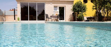 Piscina transparente com uma casa ao fundo.