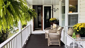 A covered porch with wicker furniture, a white railing, and potted plants.