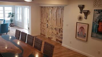 A dining area with a large wooden table and wicker chairs, a ceiling fan, and a door with a unique textured design.