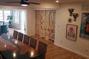 A dining area with a large wooden table and wicker chairs, a ceiling fan, and a door with a unique textured design.