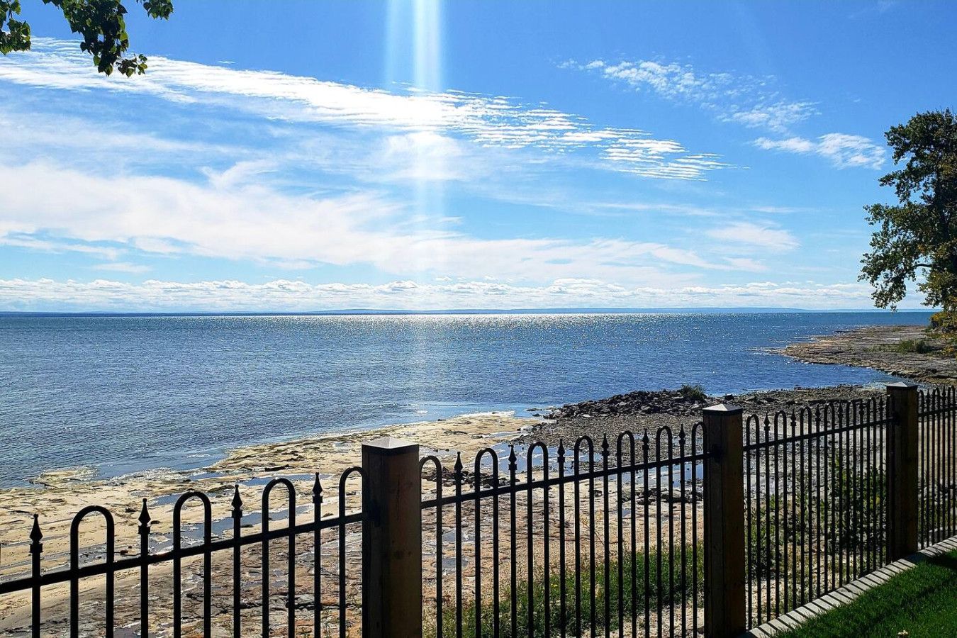 A coastal view with a clear sky, a metal fence, and a rocky shoreline.