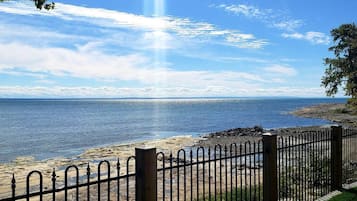 A coastal view with a clear sky, a metal fence, and a rocky shoreline.