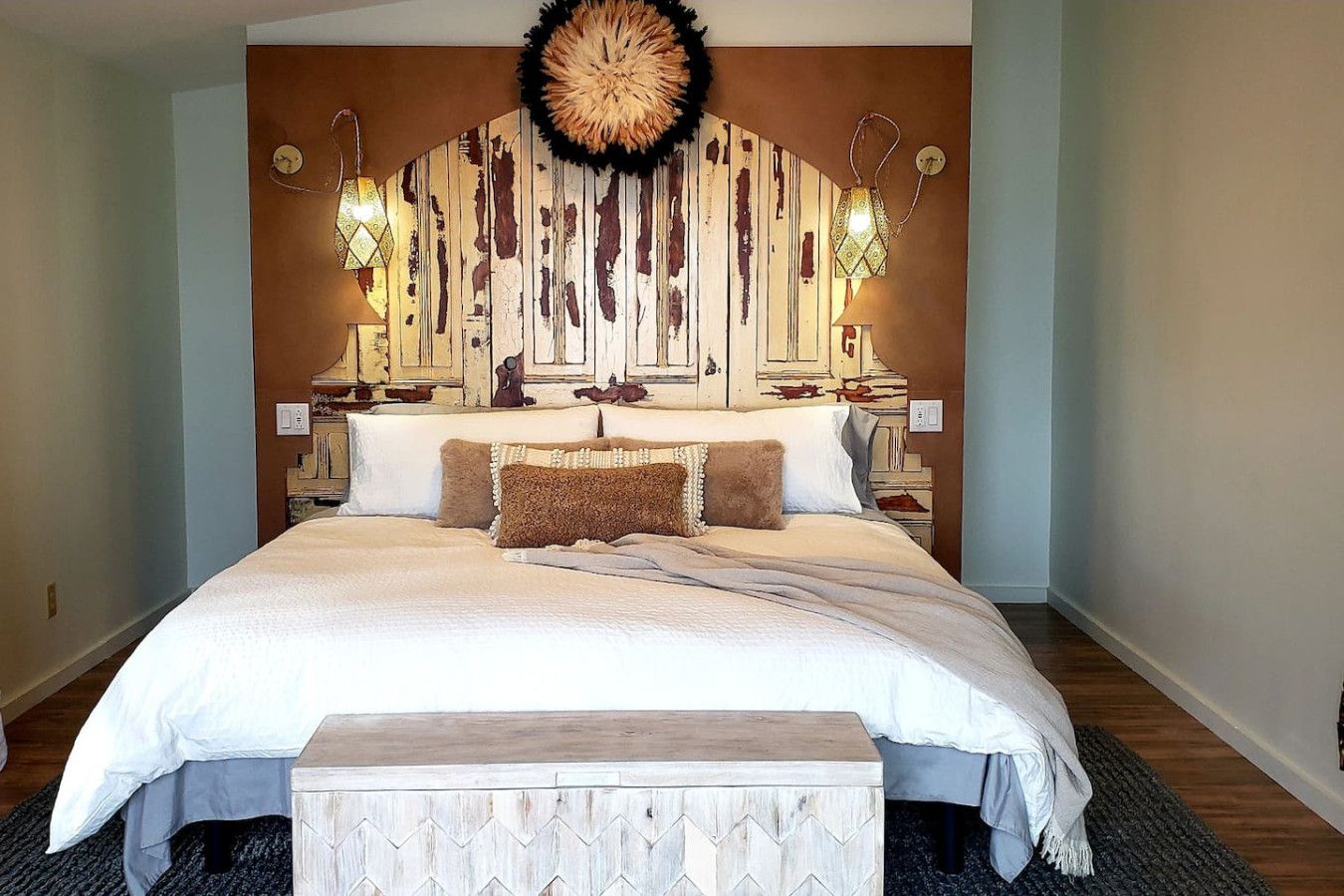 A large bed with a wooden headboard, two bedside lamps, and a decorative wall hanging.