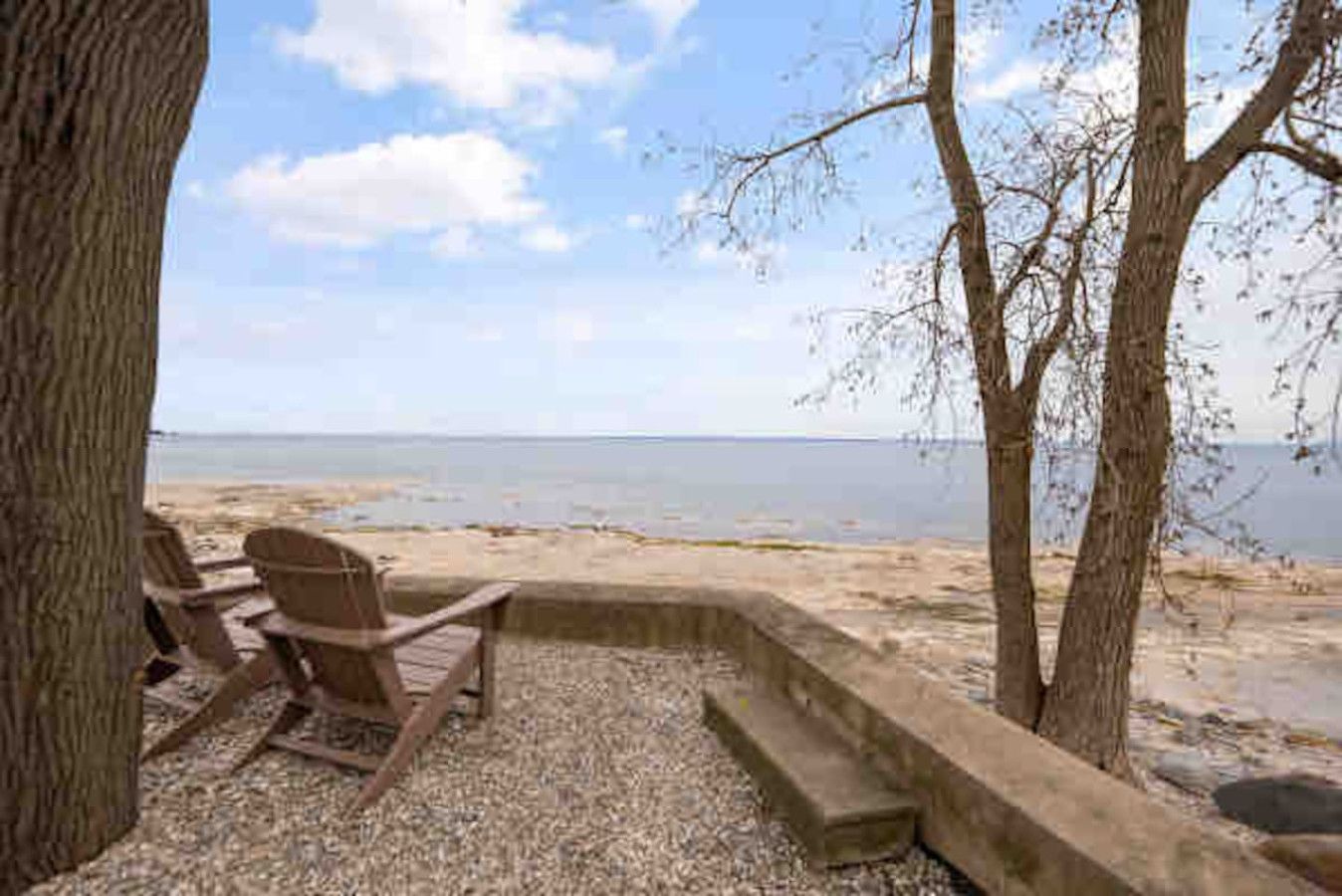 A beachside seating area with a view of the sea, a tree, and a concrete structure.
