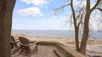 A beachside seating area with a view of the sea, a tree, and a concrete structure.
