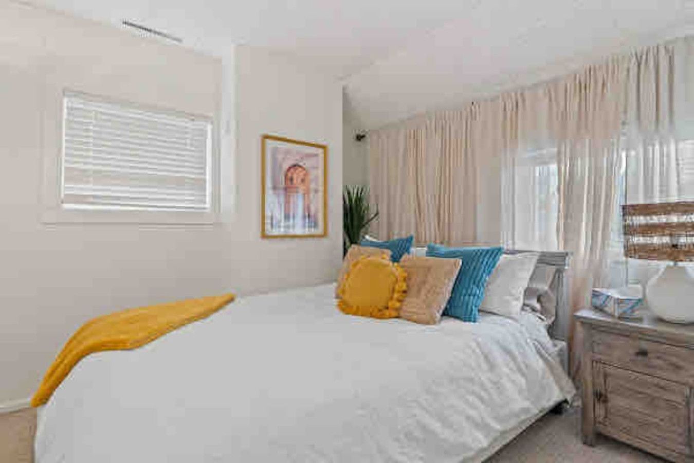 A bedroom with a bed, a bedside table, a lamp, and a window with curtains.