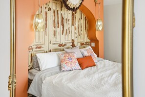A bed with white bedding and multiple pillows, a decorative headboard, and two wall-mounted lamps.