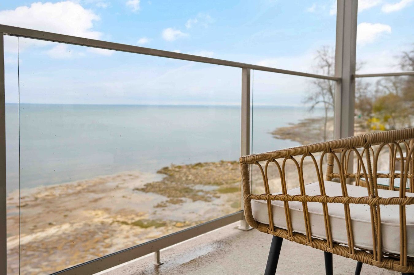 Una silla de mimbre con vista a una playa y al mar, a través de una barandilla de cristal.