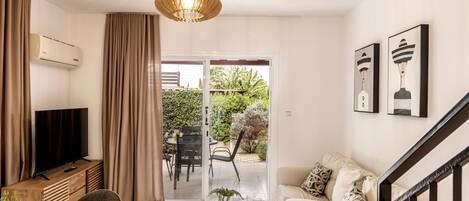 A modern living room with a sofa, a coffee table, a TV, and a balcony with outdoor furniture.